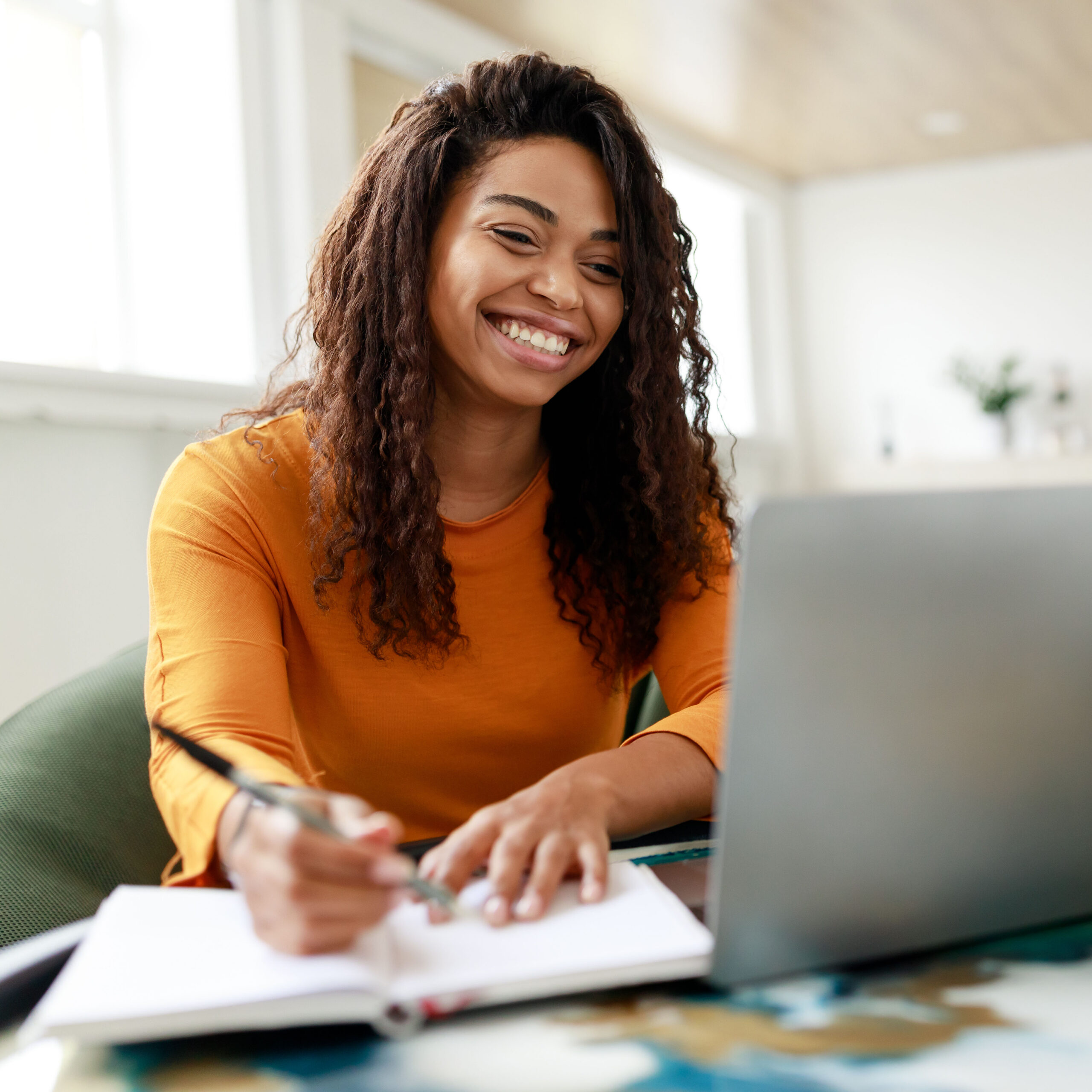 Distance Education. Portrait of smiling woman sitting at desk, using laptop and writing in notebook, taking notes, watching tutorial, lecture or webinar, studying online at home looking at screen