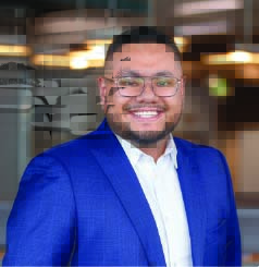 Man with beard, dark hair and glasses wearing a white dress shirt and blue sport coat