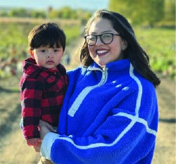 Woman holds a small boy with a field behind her