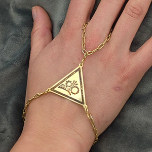 This jewelry created by Rex Herlin is a ring/bracelet combo of gold in the shape of a triangle with a delicate gold chain to wrap around wrist and middle finger.