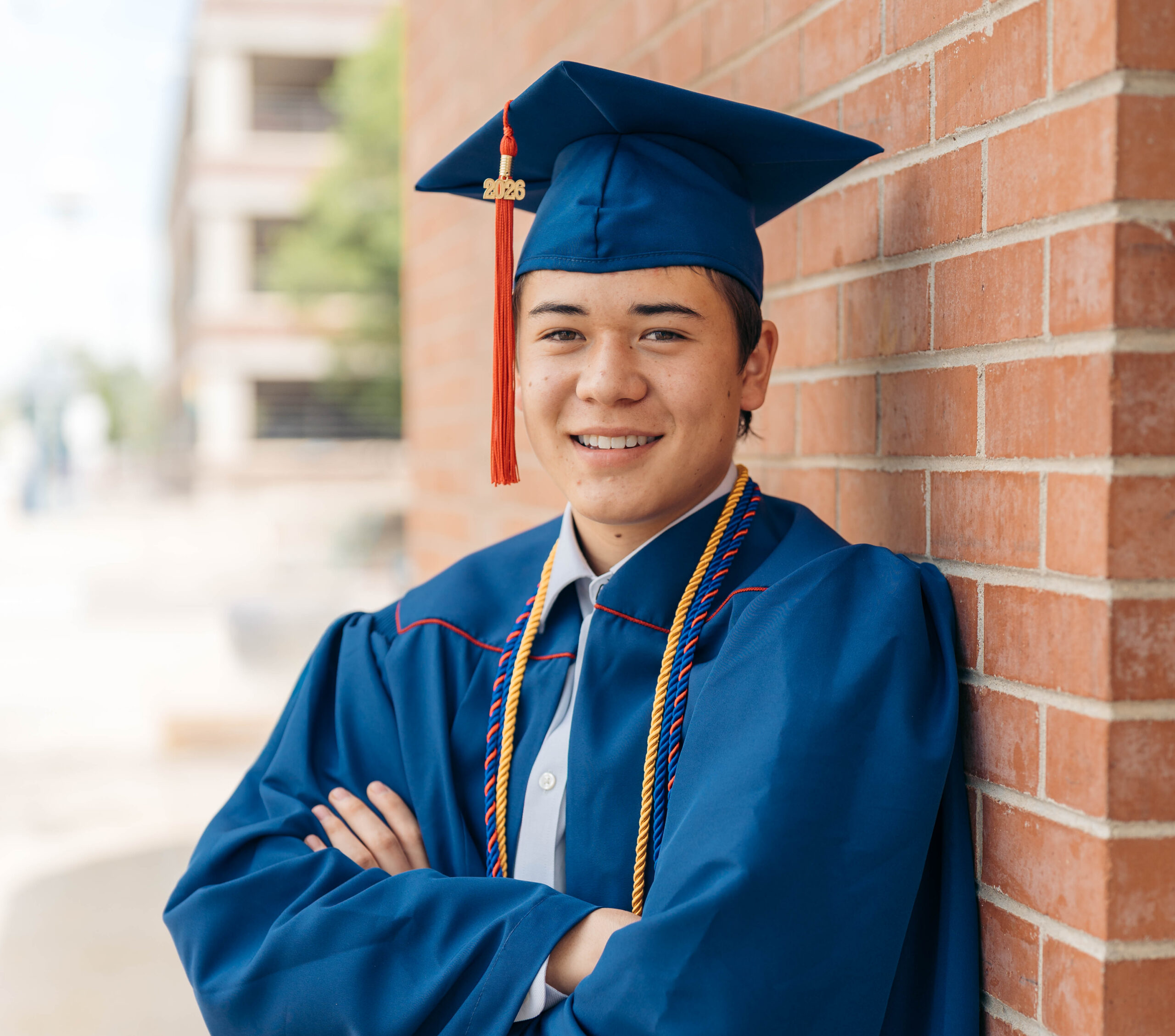 MSU Denver graduate in graduation outfit leaning on brick wall.