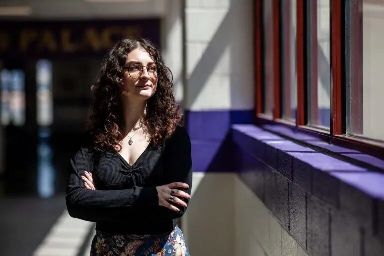 Student standing in hallway looking out windows.