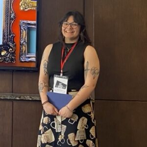A woman with brown hair and glasses wearing a badge on a lanyard