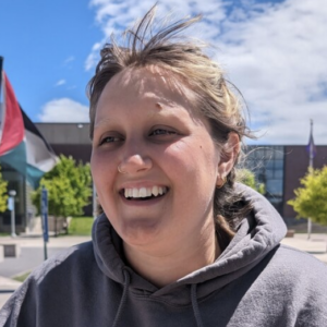 A person with light brown hair smiling and wearing a gray hoodie