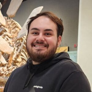 A man with brown hair and a beard wearing a black hoodie
