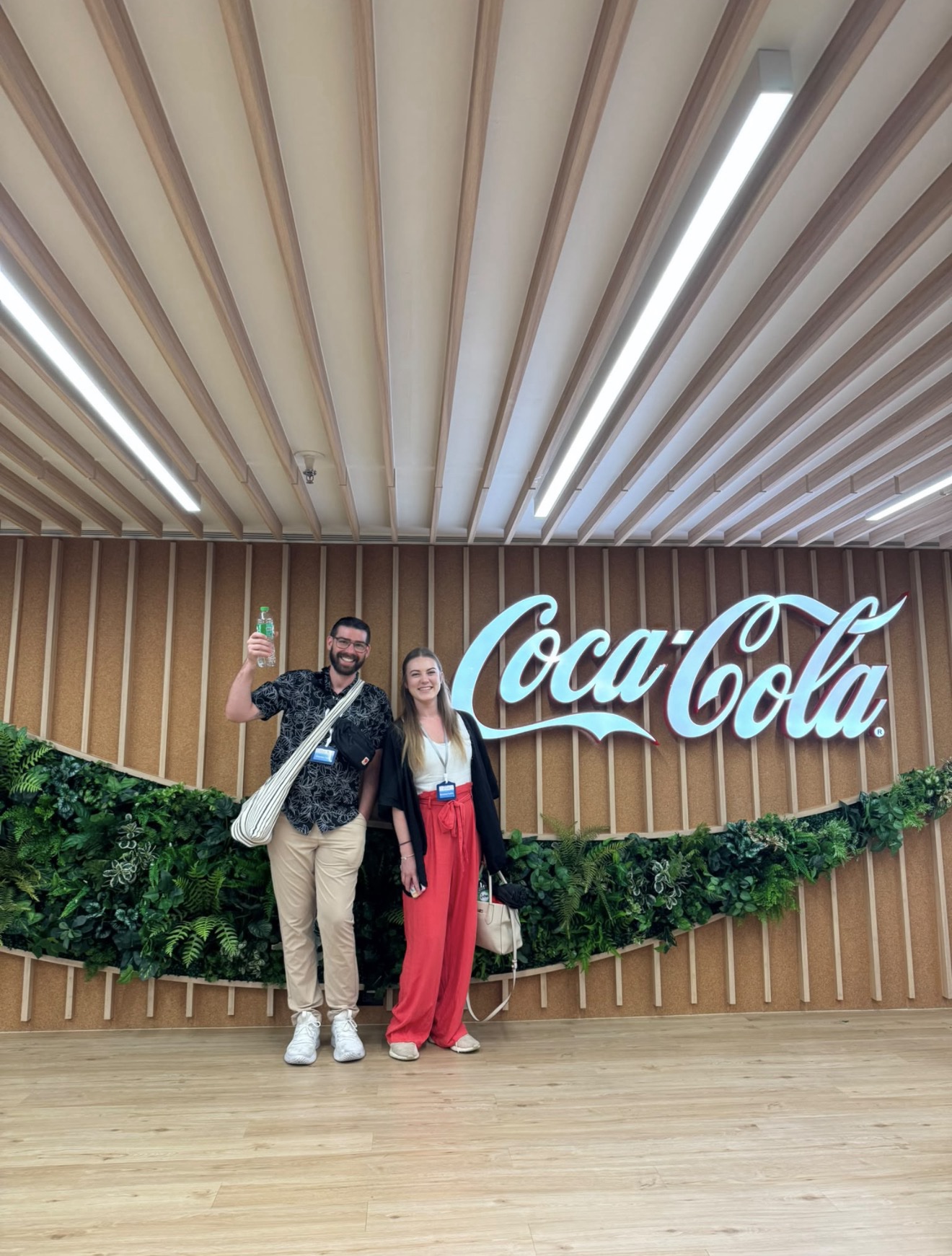 A man and a woman pose together in front of a modern wood-paneled wall featuring a large, illuminated white 