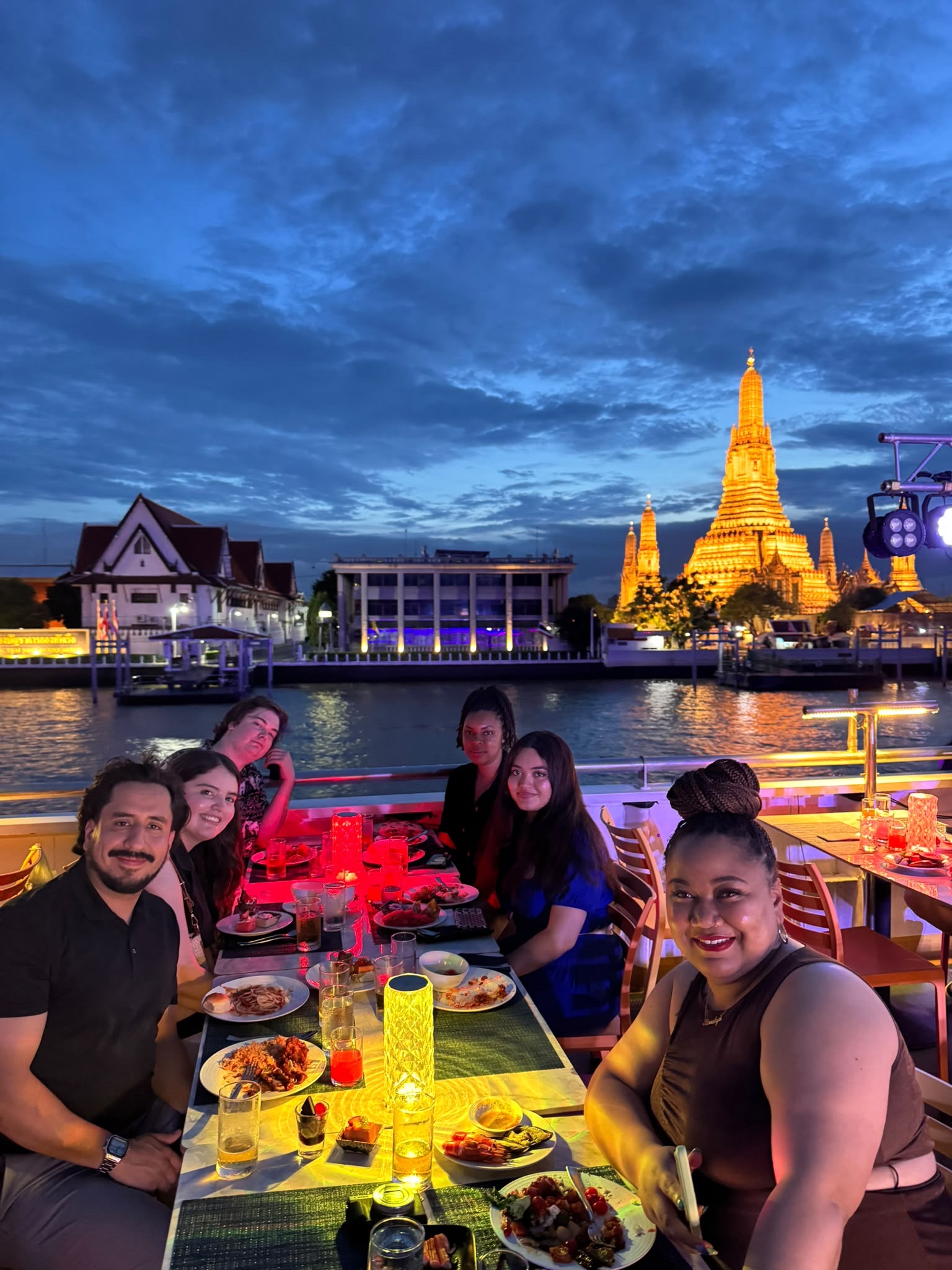A group picture of students on a cruise ship with a temple in the background and water.