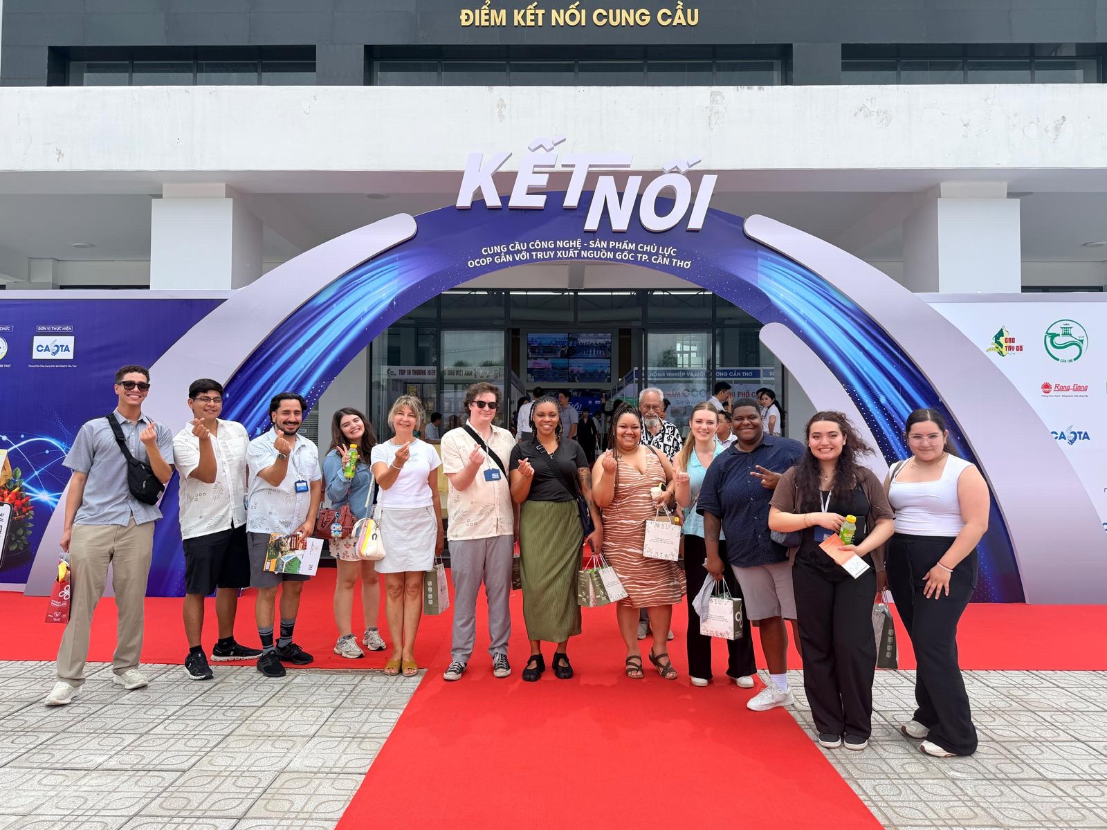 A group photo of the MSU Denver student delegation standing together on a red carpet under a wide archway entrance featuring a blue graphic with the Vietnamese text 