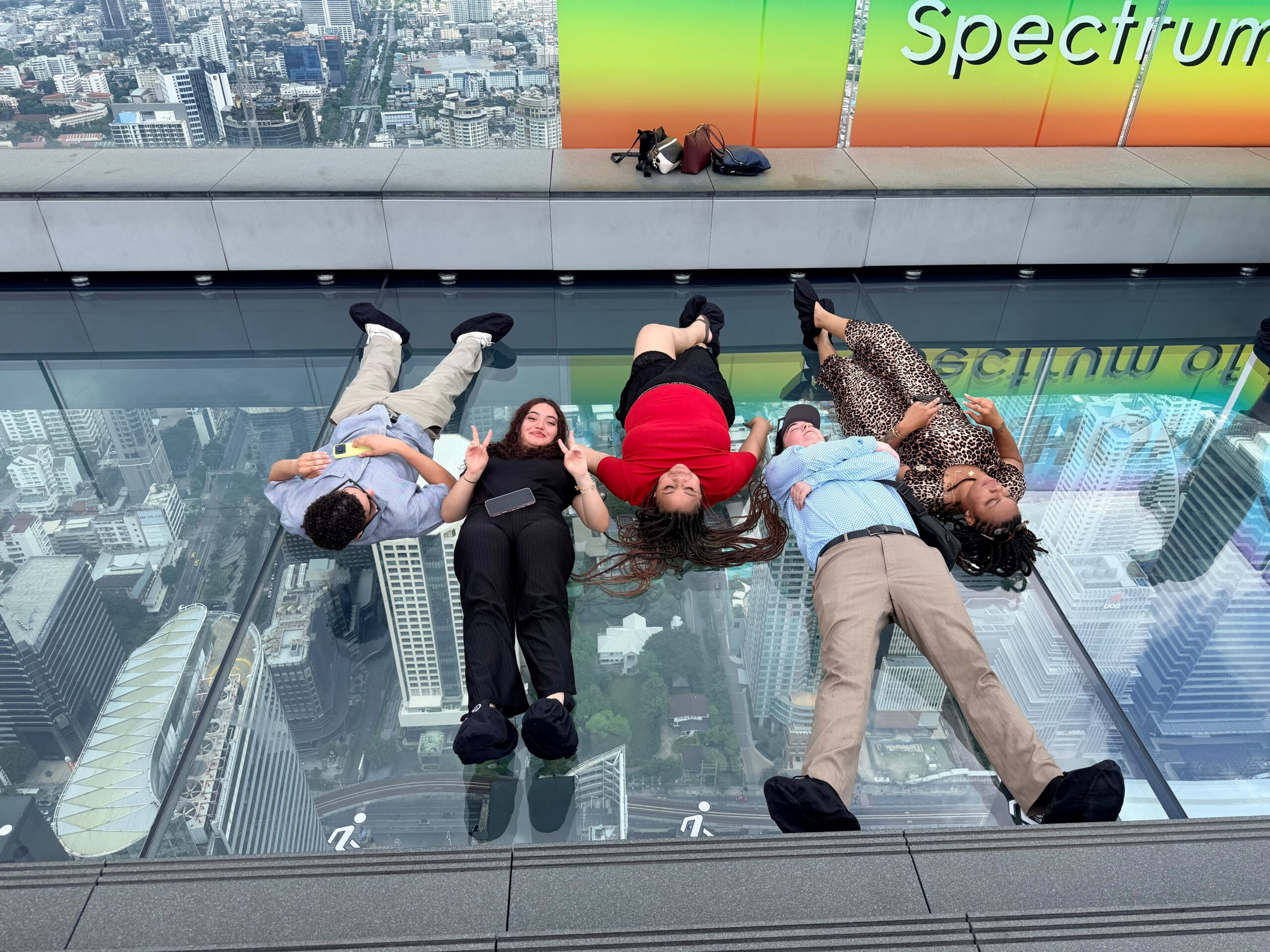 Students laying down over the skyline ridge in Bangkok Thailand smiling.