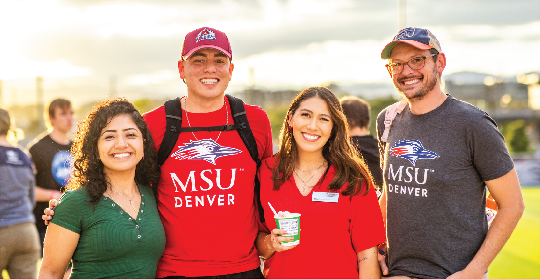 Four community members smile with the sunsetting behind them.