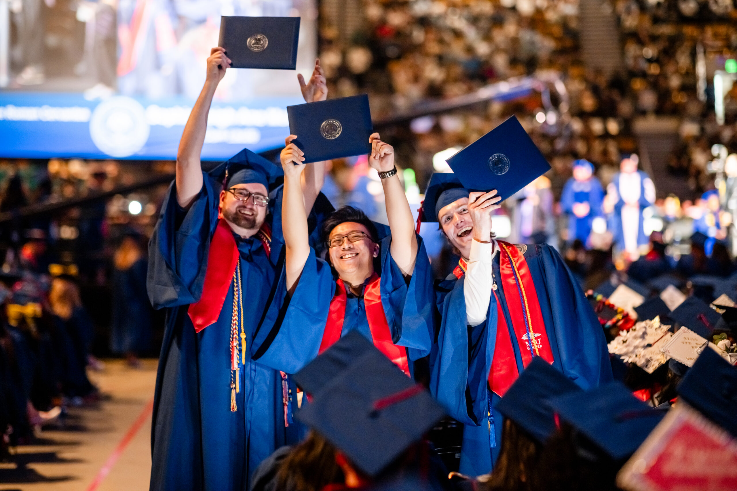 3 accounting grads hold up their diploma covers in excitement after crossing the stage at the SP'26 Commencement Ceremony