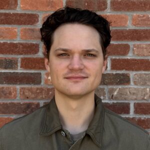 A man with short dark hair wearing a green collared shirt
