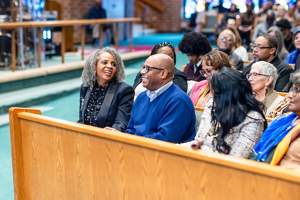 A group of people sitting in a church. With a man and woman talking to each other.