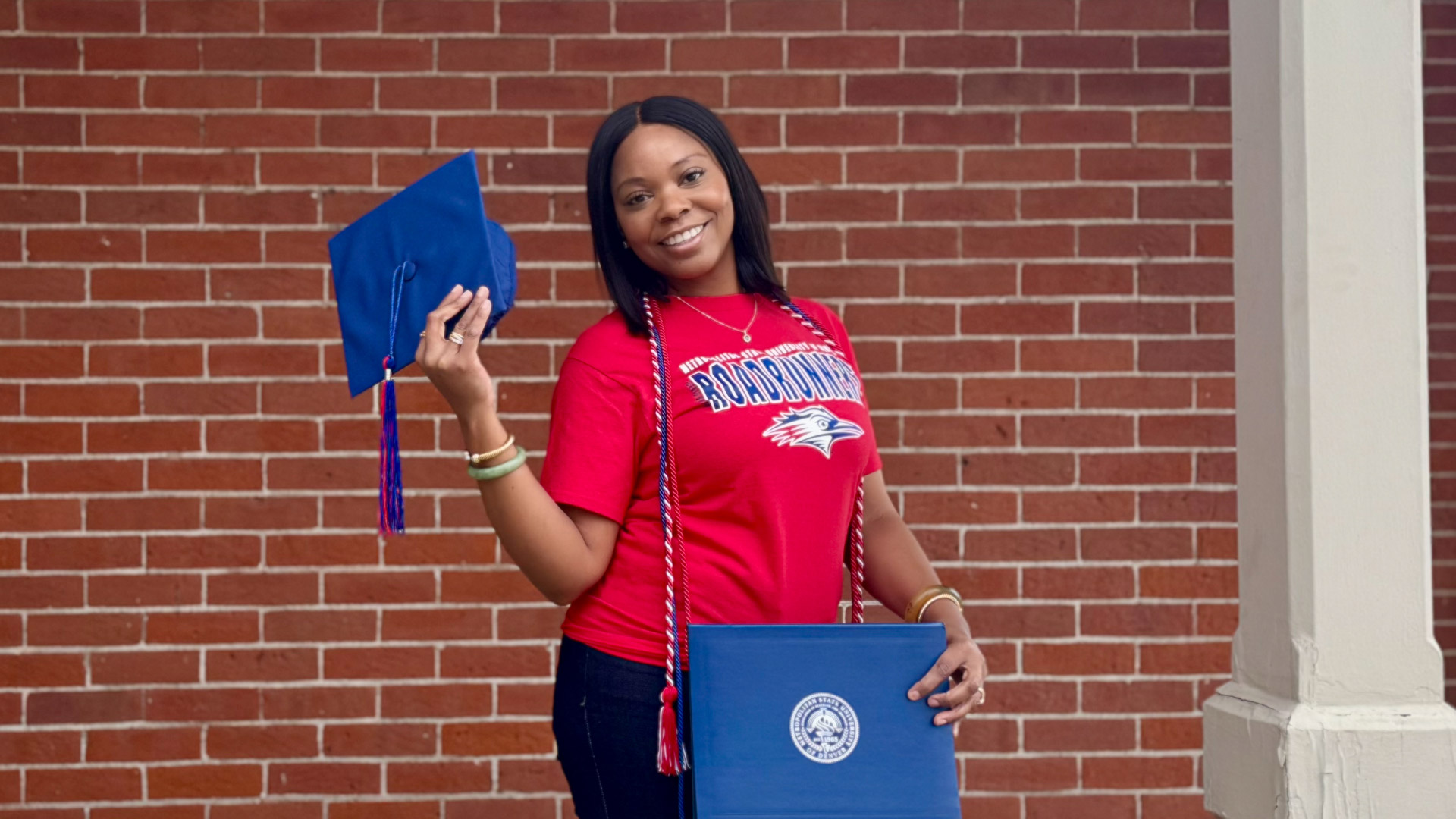 Stacy Berry standing in front of a brick wall holding her diploma and graduation cap