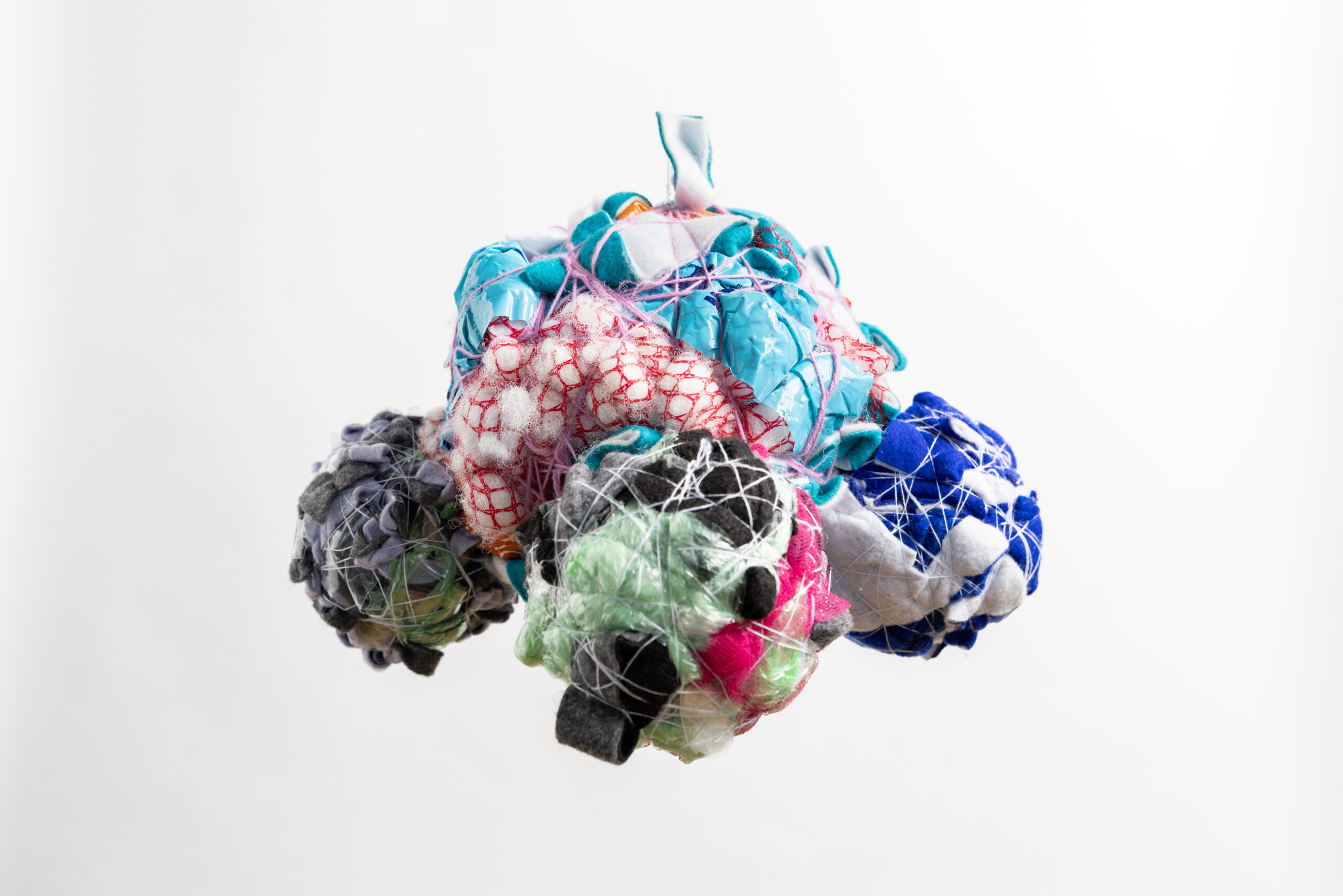 Cluster of colorful fabric bundles wrapped in netting against a white background.