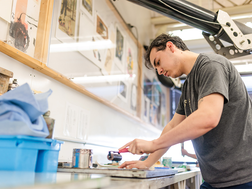 A student prepares to roll printmaking media.