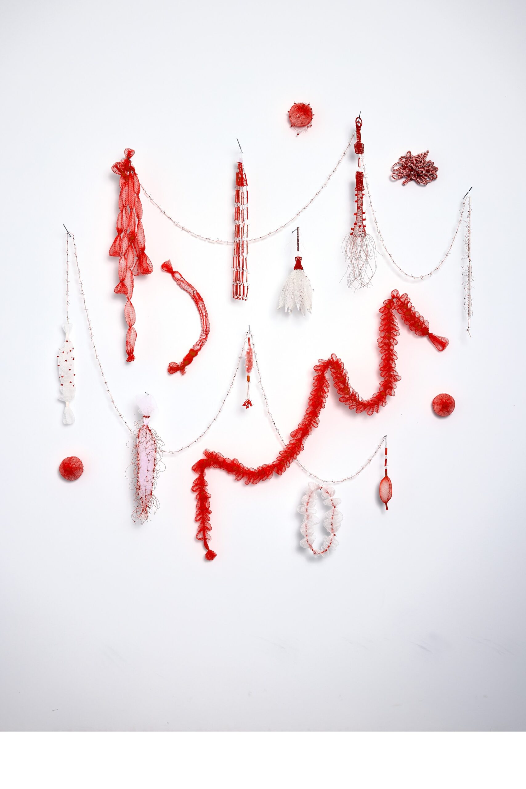 An artistic display of red and white decorative objects arranged on a white background, featuring various textures and shapes including lace, beads, and circular elements.