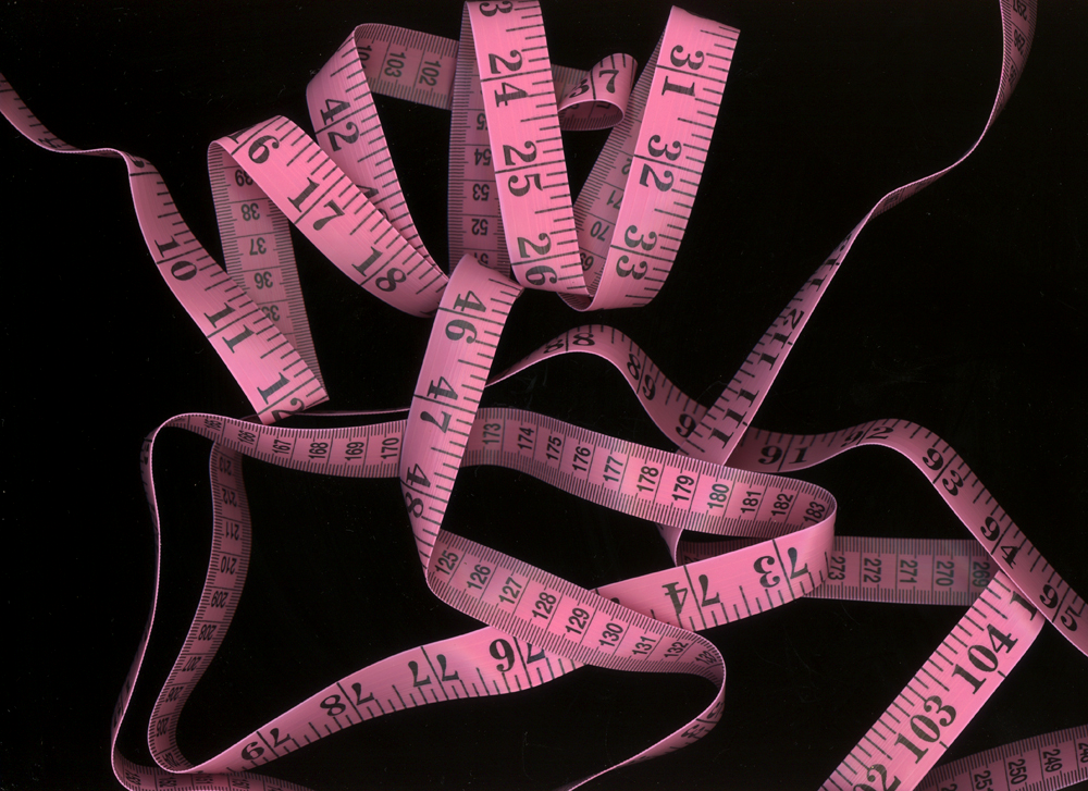 A chaotic arrangement of pink measuring tapes against a dark background, displaying black measurement markings.