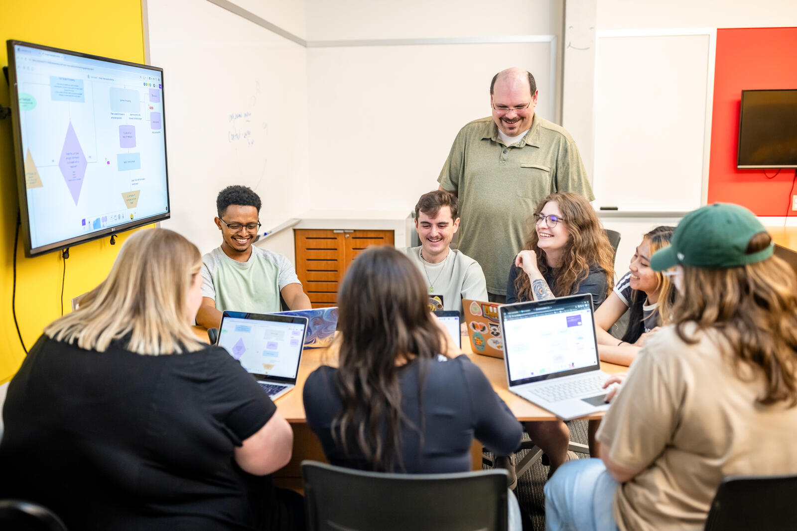 Dr. Daniel Pittman and a team of C3 Lab student researchers working on laptops around a table, with a project workflow diagram displayed on the screen behind them