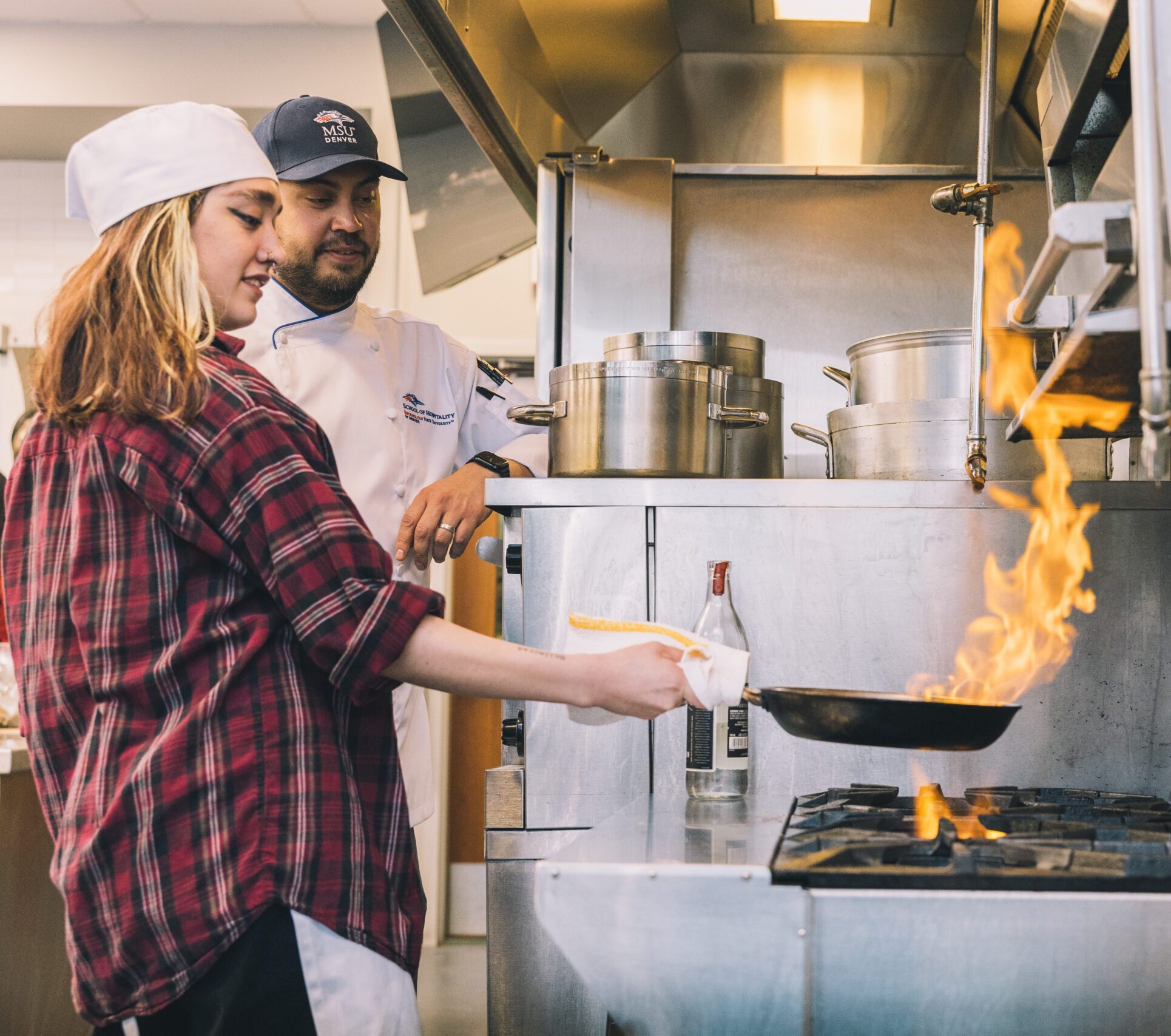 student and professor cooking food over a stove with a big flame