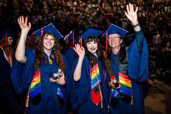 Three graduates throw their hands in the air with excitement as they celebrate that Commencement day has finally come!
