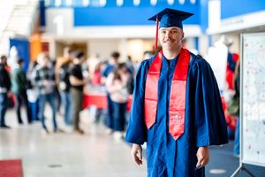 A grad smiles for the camera while dressed up in MSU Denver branded commencement regalia.