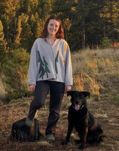 Elizebeth Paur in front of a forest and mountains with her black dog