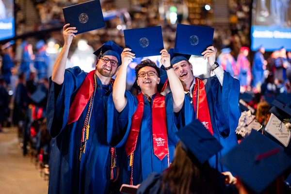 Three grads get close to pose for the camera as they display their diploma covers