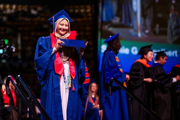 A grad smiles and holds their diploma cover up as they exit the Commencement stage