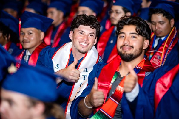 Two graduates give a thumbs up as they smile for the camera
