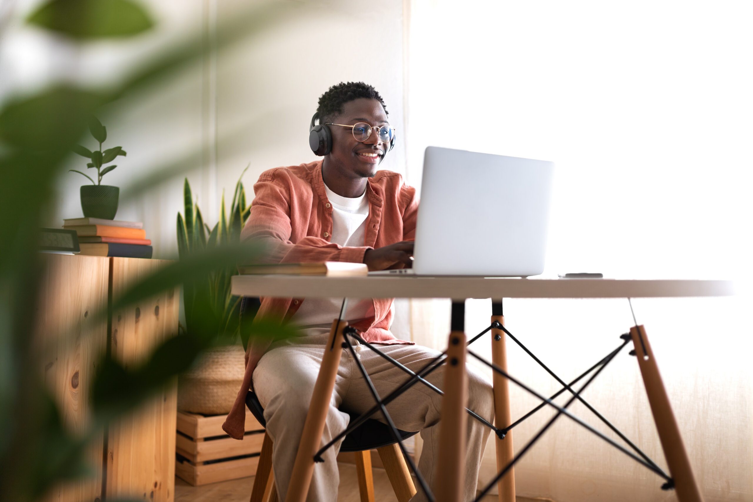 person with short black hair, glasses, and dark skin wears headphones while sitting in front of a laptop