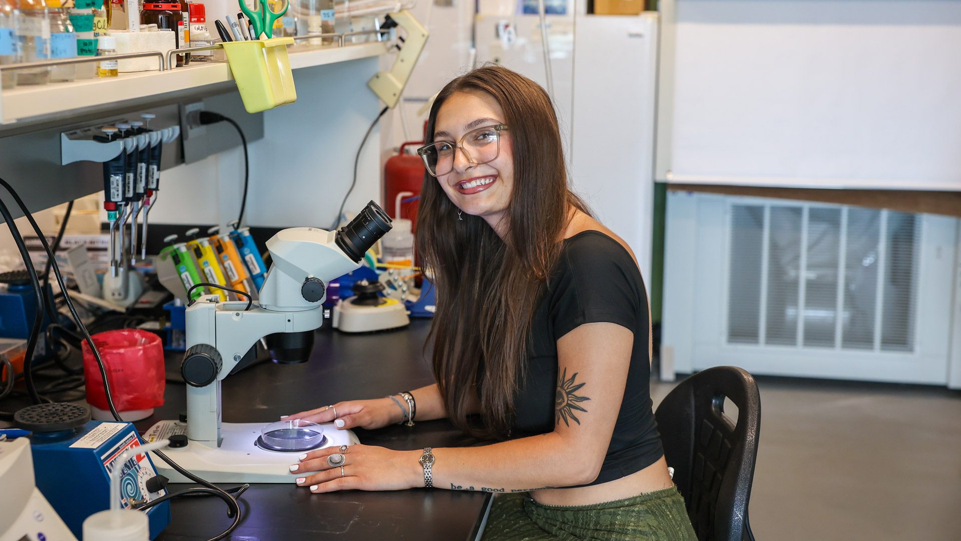 MSU Denver student Elena Herrera smiling in front of a microscope in a lab on campus