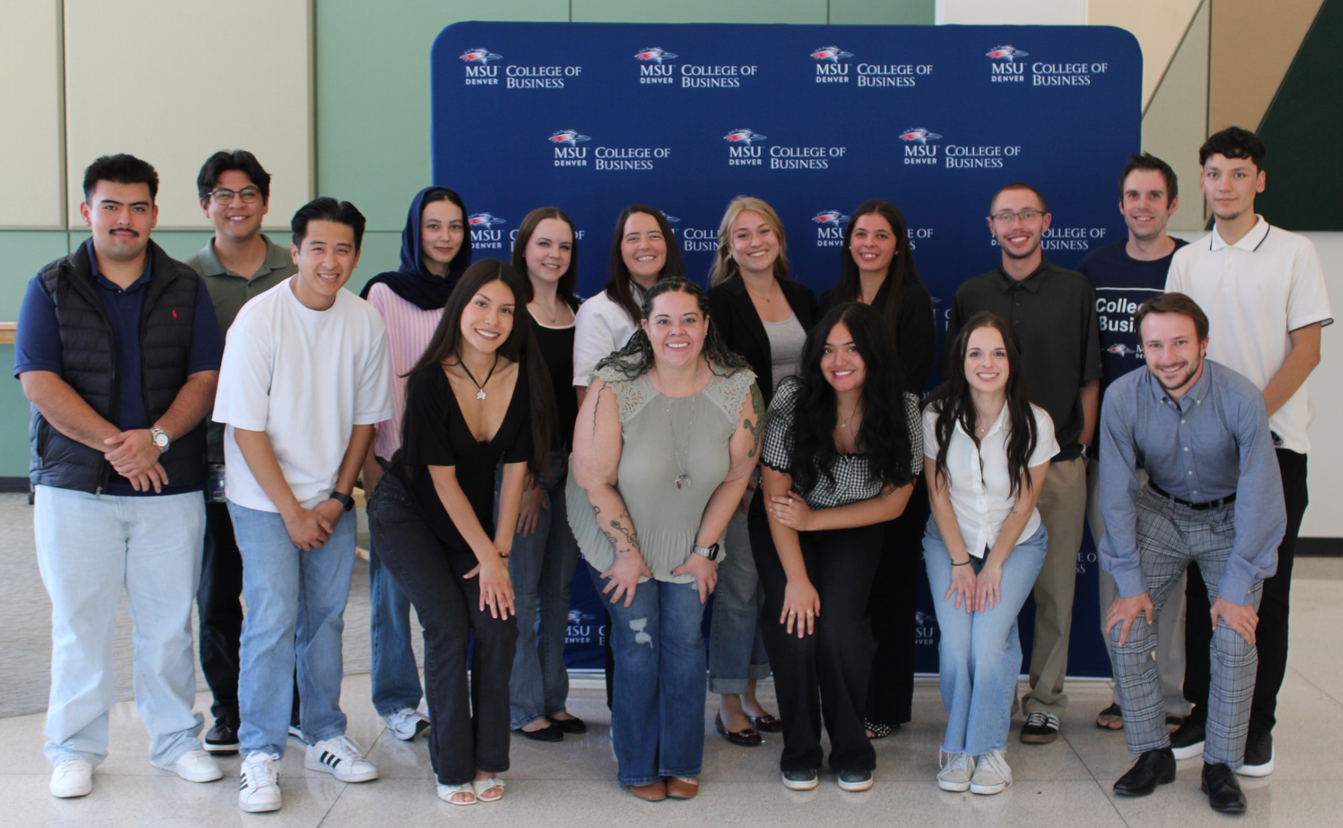 A group of students poising for a photo in front of the College of Business step n repeat