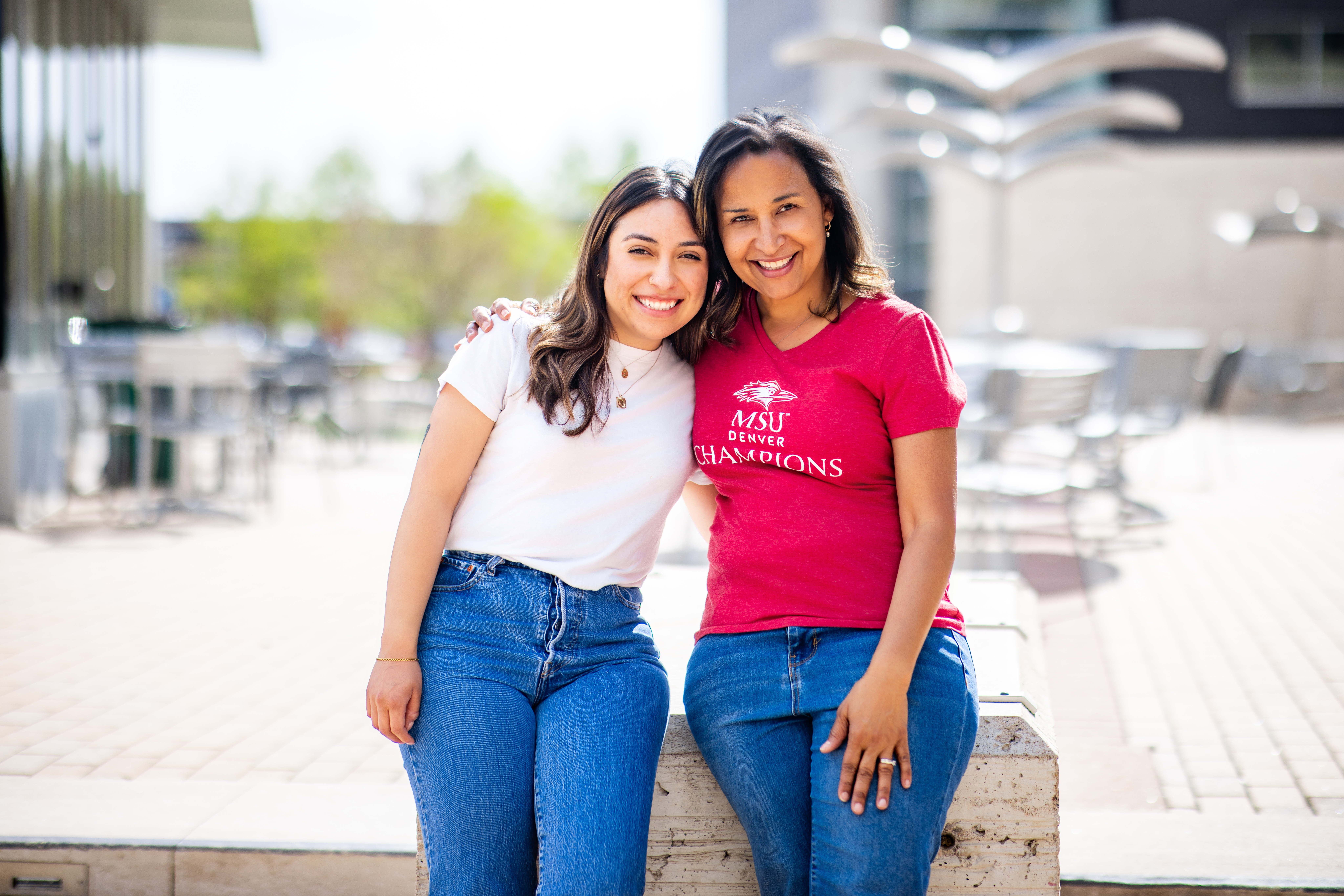 Two students smiling and sitting on a rock bench