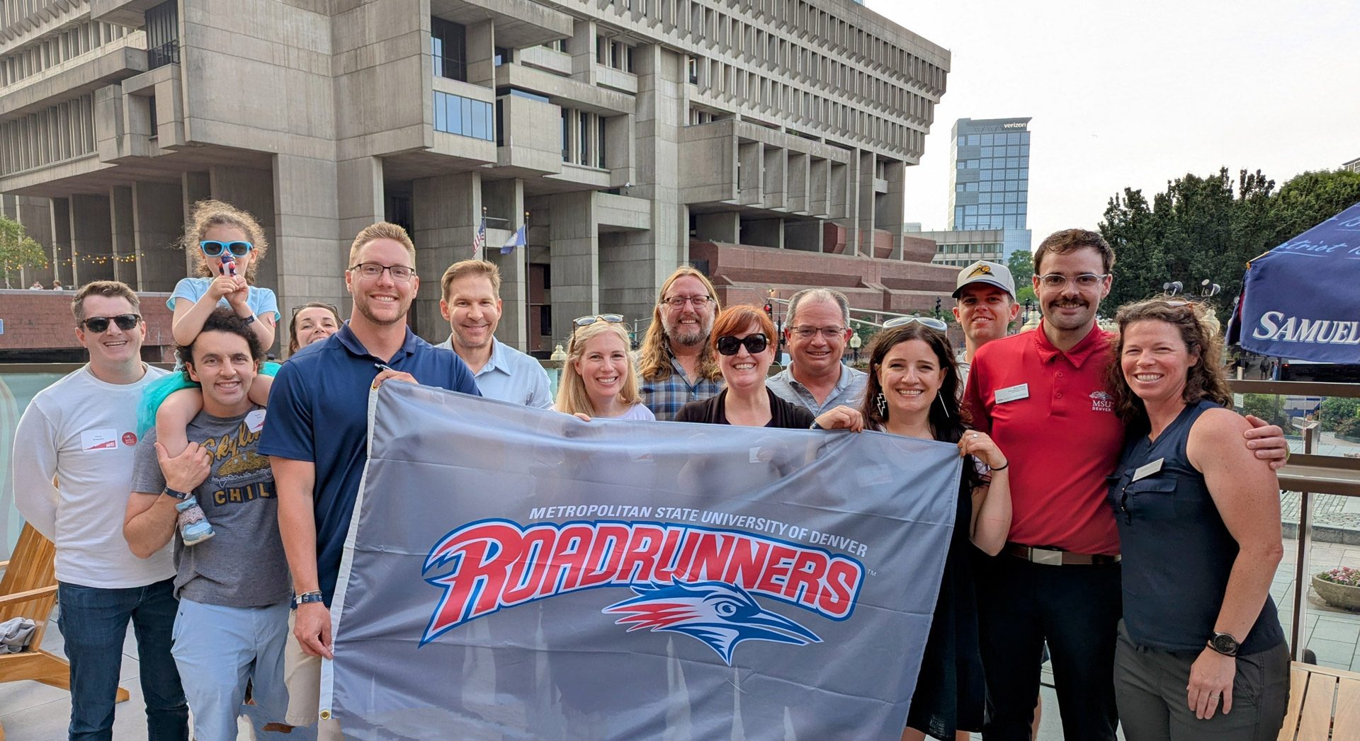A group of MSU Denver alumni at a Roadrunners Roadshow event with a Roadrunners flag