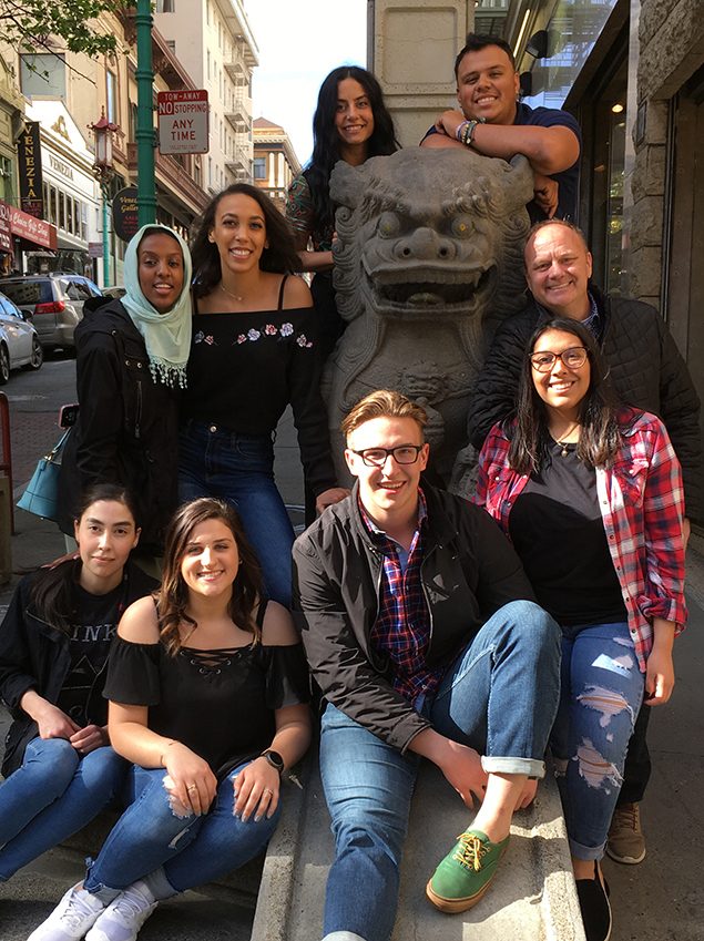 Richard Moeller and eight Model UN students in 2019, posing beside a stone lion statue on a city sidewalk.