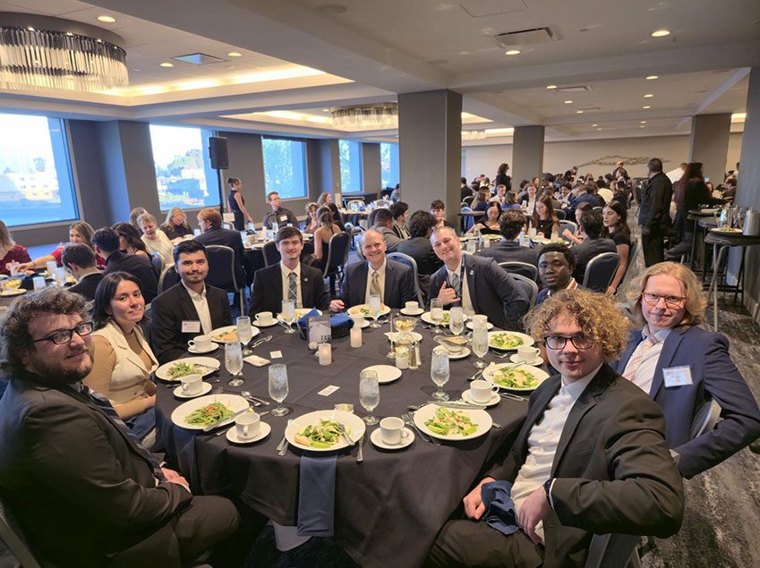 Richard Moeller and Model UN students in 2025, dressed in business attire and seated at a round table during a banquet in a hotel ballroom.