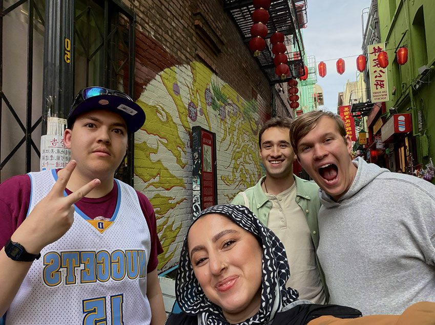 Four Model UN students in 2026, smiling in a group selfie in an alley hung with red lanterns, beside a painted mural.