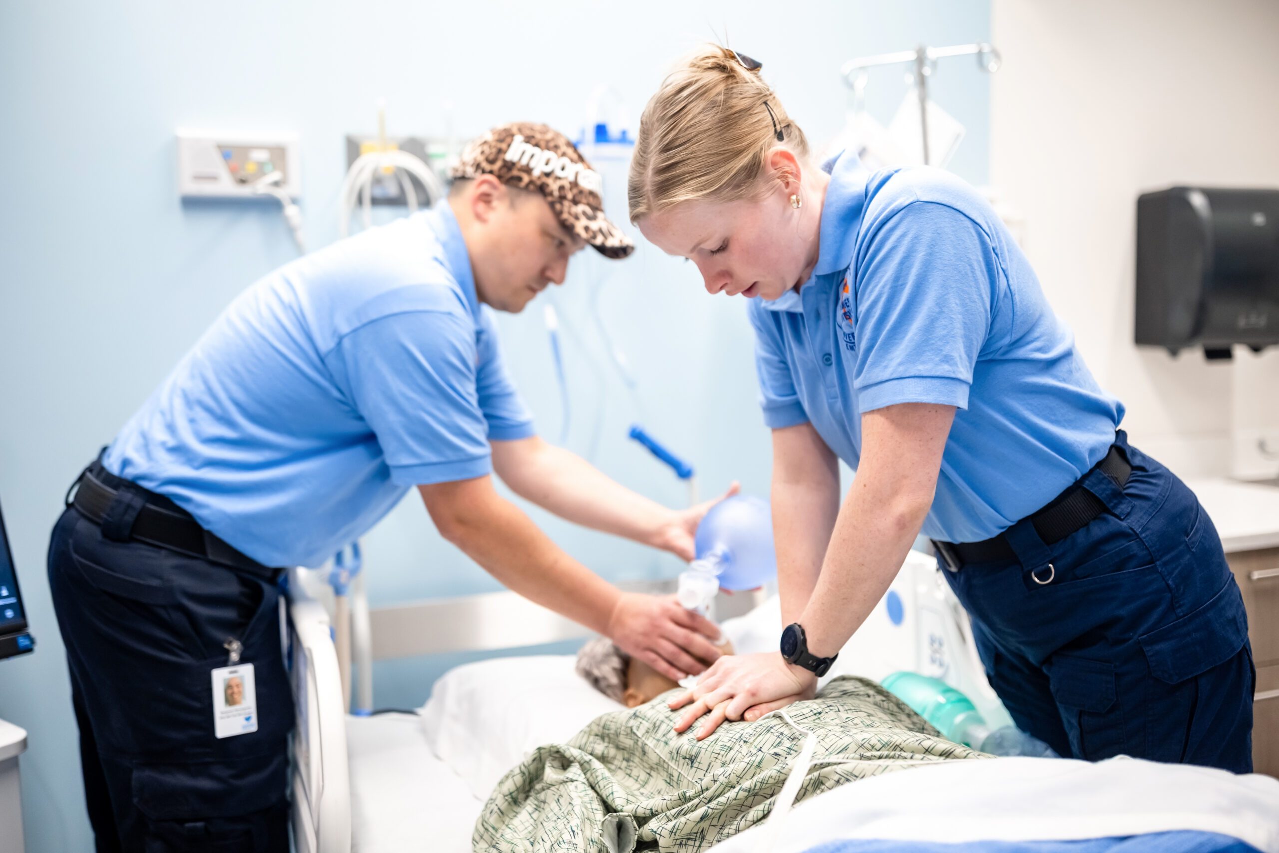 Two EMT students in blue shirts working on a practice patient.