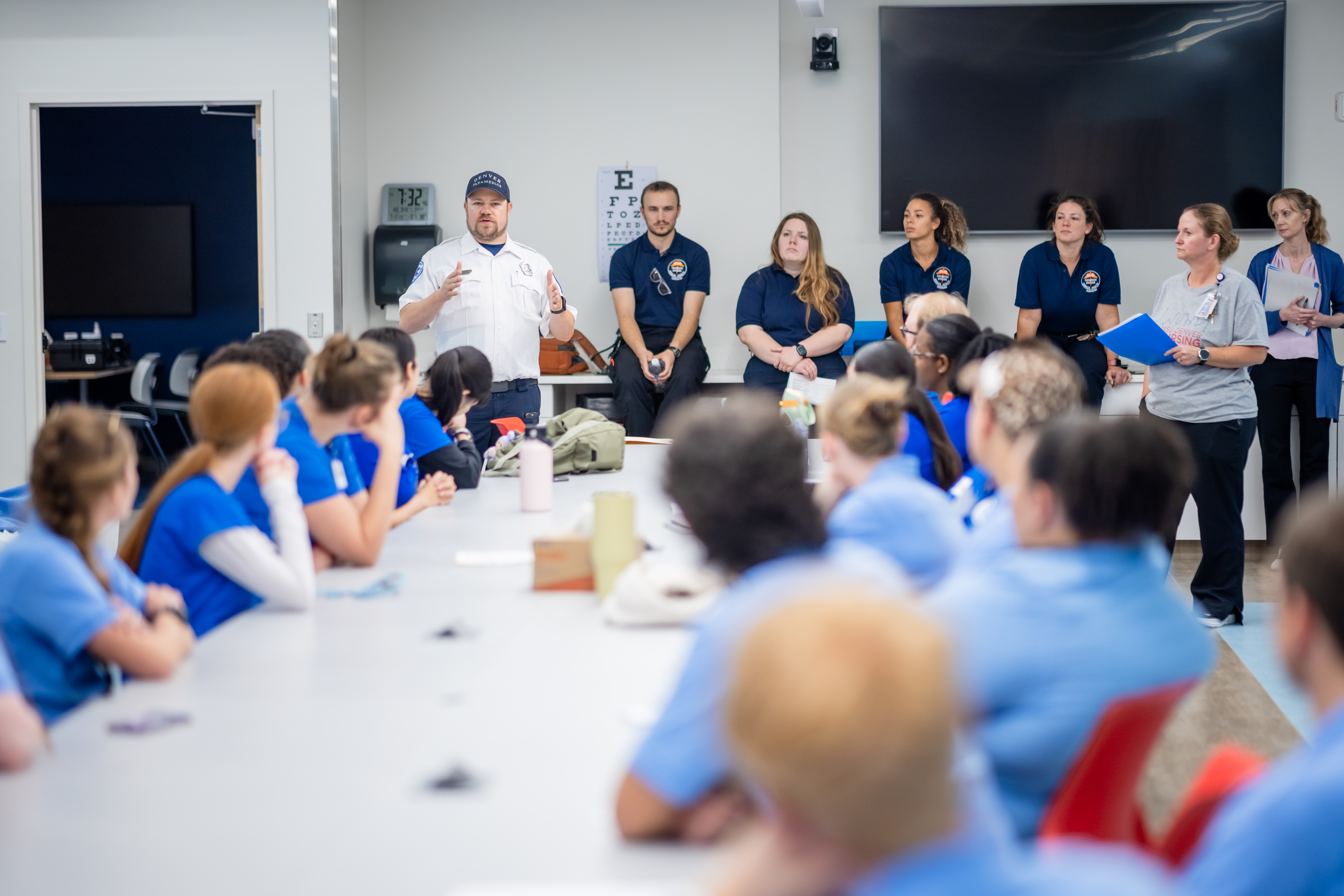 Students sitting at a long table listening to EMT instructor speak.