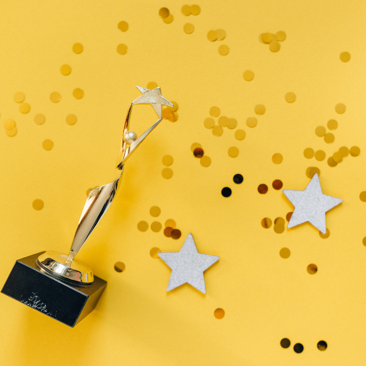 A gold trophy on a yellow background with glitter and star confetti.